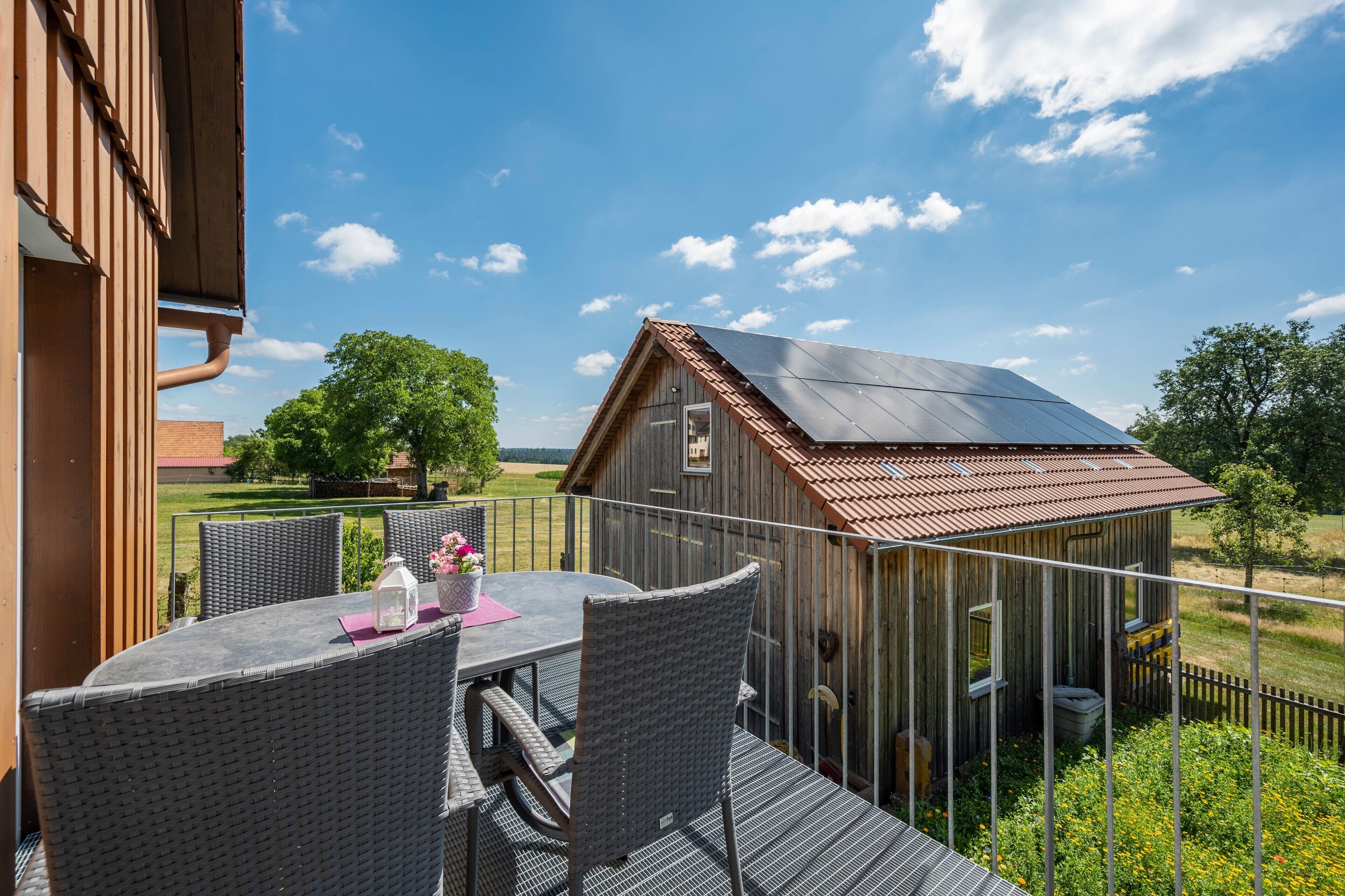 Une terrasse en bois avec une table et des chaises, un petit abri de jardin et un ciel dégagé.