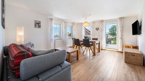 Een moderne woonkamer met een grijze bank, een eettafel met stoelen en een balkon met uitzicht.