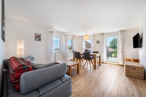 Ein modernes Wohnzimmer mit einem grauen Sofa, einem Esstisch mit Stühlen und einem Balkon mit Blick.