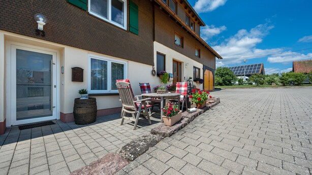 Een woongebouw met een geplaveid terras, buitenmeubels en een zonnepaneelinstallatie.