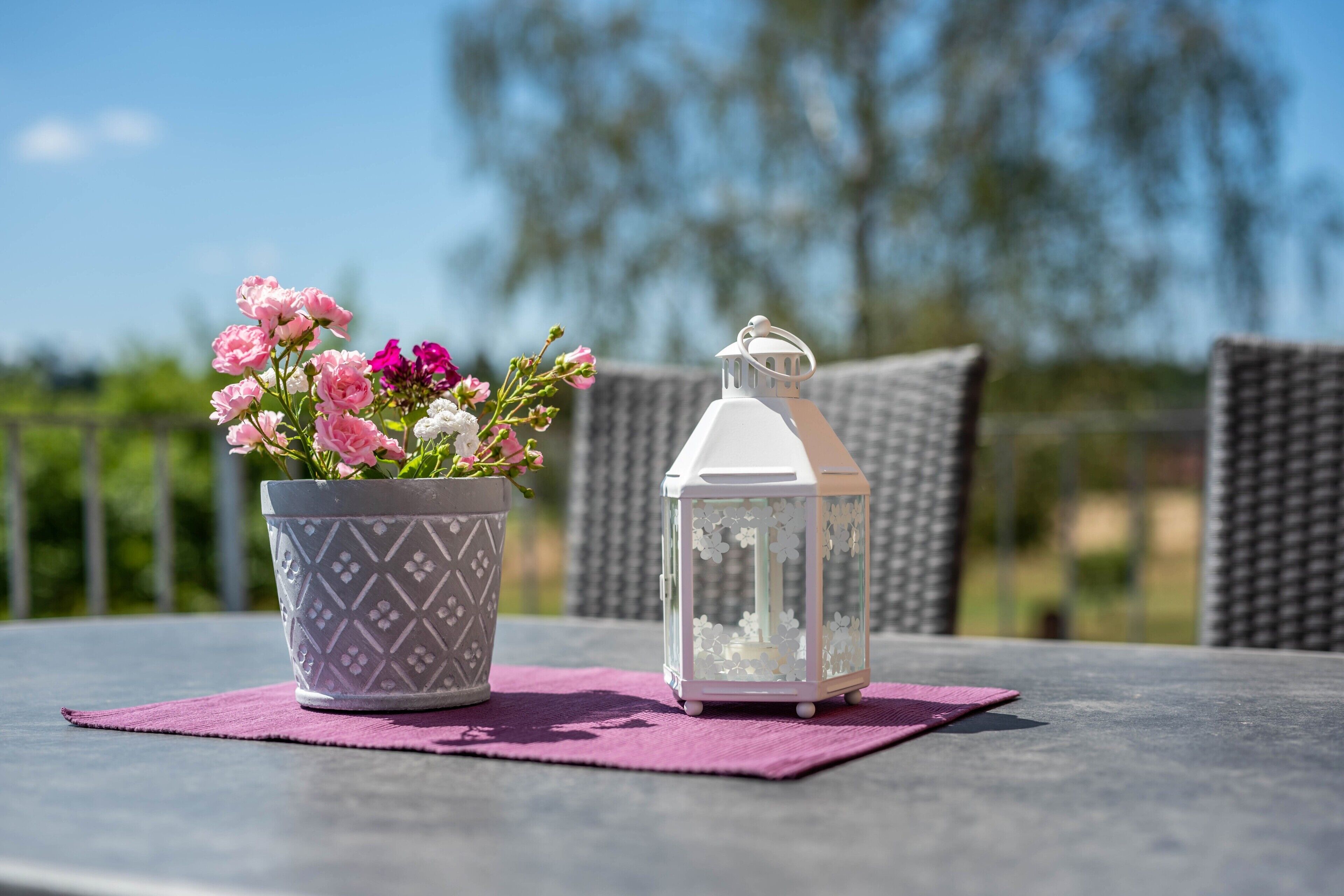 A potted plant with flowers and a white lantern on a table.