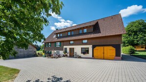 Een gebouw met twee verdiepingen, een pannendak, een geplaveid oprit en een voortuin.