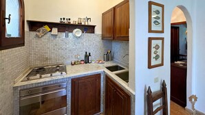 Een keuken met een gasfornuis, oven en spoelbak, houten kastjes, een betegelde achterwand en wanddecoratie bestaande uit ingelijste afbeeldingen van vissen.