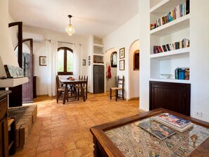 A spacious living area with a dining table, chairs, a bookshelf, and a patterned rug.