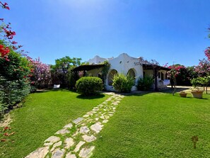 A white building with arches, a stone pathway, and lush greenery.