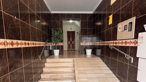 Ein Flur mit einer Treppe, dunklen Fliesenwänden und einer Deckenleuchte.