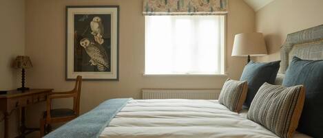 Un dormitorio con cama, ventana con cortinas, lámpara, silla y un cuadro en la pared.