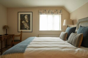 A bedroom with a bed, a window with curtains, a lamp, a chair, and a framed picture on the wall. - Crown and Anchor Ham (Marlborough)