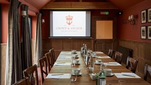 A conference room with a long table set for a meeting, a screen displaying 'CROWN & ANCHOR' branding, wooden paneling, and framed pictures on the walls. - Crown and Anchor Ham (Marlborough)
