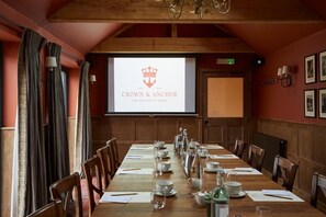 A conference room with a long table set for a meeting, a screen displaying 'CROWN & ANCHOR' branding, wooden paneling, and framed pictures on the walls. - Crown and Anchor Ham (Marlborough)