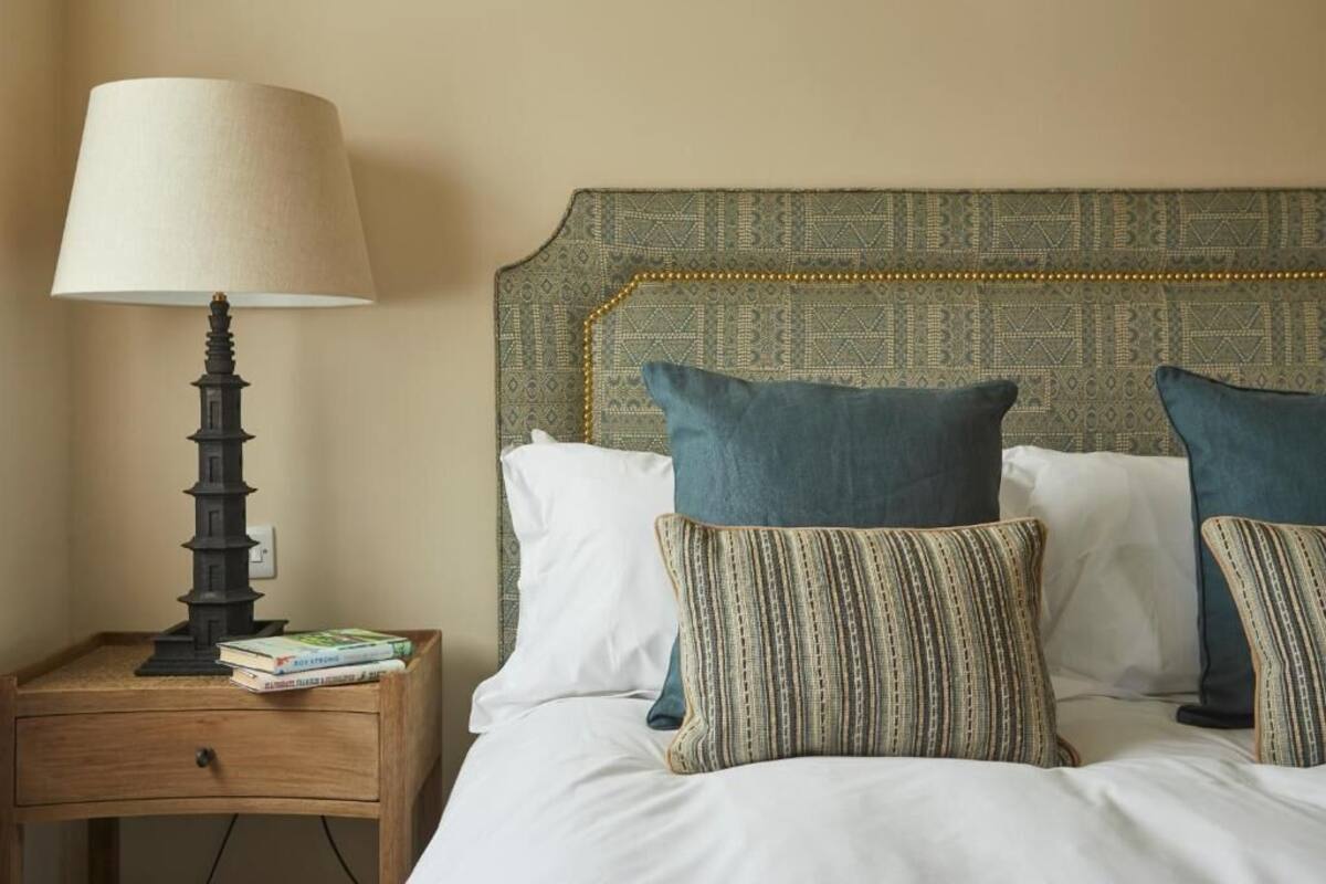 A neatly made bed with pillows, a bedside lamp, and a small wooden nightstand with books.