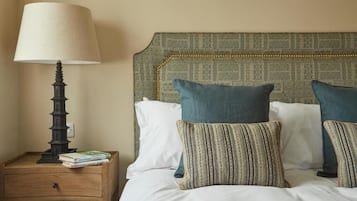 A neatly made bed with pillows, a bedside lamp, and a small wooden nightstand with books.