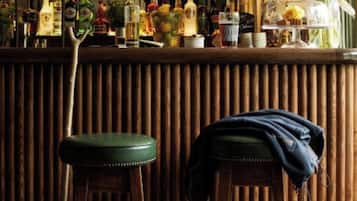A bar area with stools, a wooden counter, and a variety of bottles.