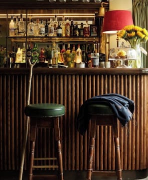 Een bar met krukken, een houten toonbank en verschillende flessen.
