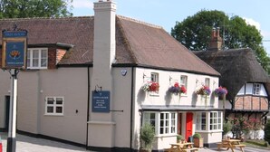 A traditional building with a red door, outdoor seating, and flower baskets. - Crown and Anchor Ham (Marlborough)