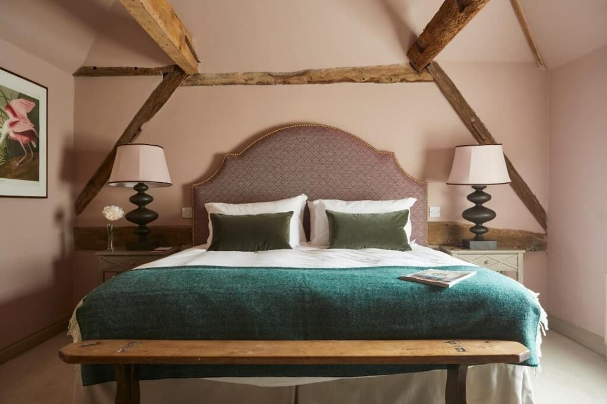 A bed with a wooden headboard, two bedside lamps, a green bedspread, and a nightstand with a vase of flowers.