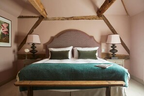 A bed with a wooden headboard, two bedside lamps, a green bedspread, and a nightstand with a vase of flowers. - Crown and Anchor Ham (Marlborough)