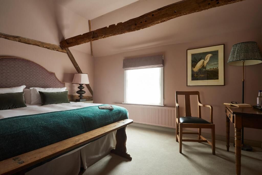 A bedroom with a bed, a chair, a desk, a lamp, a window, and a painting.