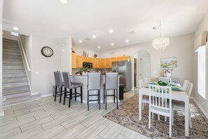 A modern kitchen with a dining area, wooden cabinets, a stainless steel refrigerator, and a chandelier. - Games Room Pool Home on Lazy Breeze Loop (Clermont)