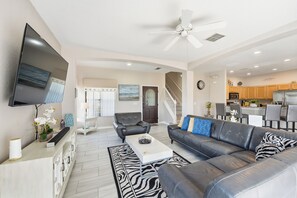 A modern living room with a flat-screen TV, leather sofas, a coffee table, and a staircase leading to the kitchen. - Games Room Pool Home on Lazy Breeze Loop (Clermont)