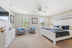A bedroom with a bed, a desk, two chairs, a ceiling fan, and large windows. - Games Room Pool Home on Lazy Breeze Loop (Clermont)