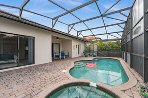 Ein überdachter Pool mit Pflasterterrasse, eine Glastür, die zu einem Raum führt, und eine Metall-Dachkonstruktion.