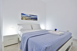 A bedroom with a bed, a nightstand, a drawer, a painting on the wall, and a window. - A cozy apartment perfect for two people, located on the ground floor of a building near the Spanish Quarter, on the highest part of the hill and close to the Corso Vittorio Emanuele funicular. Comfortable and simple, with a direct entrance to the kitchen (Naples)