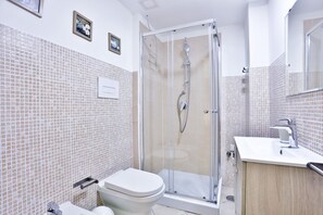 A modern bathroom with a glass-enclosed shower, a toilet, and a sink with a mirror. - A cozy apartment perfect for two people, located on the ground floor of a building near the Spanish Quarter, on the highest part of the hill and close to the Corso Vittorio Emanuele funicular. Comfortable and simple, with a direct entrance to the kitchen (Naples)