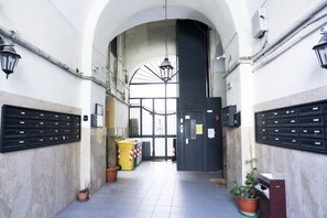 An arched hallway with mailboxes, a trash bin, and potted plants. - A cozy apartment perfect for two people, located on the ground floor of a building near the Spanish Quarter, on the highest part of the hill and close to the Corso Vittorio Emanuele funicular. Comfortable and simple, with a direct entrance to the kitchen (Naples)