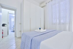 A hotel room with a bed, a wardrobe, a bathroom visible through an open door, and a window with sheer curtains. - A cozy apartment perfect for two people, located on the ground floor of a building near the Spanish Quarter, on the highest part of the hill and close to the Corso Vittorio Emanuele funicular. Comfortable and simple, with a direct entrance to the kitchen (Naples)