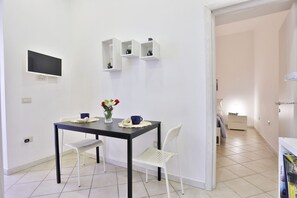 A room with a table, chairs, a TV, and a bed. - A cozy apartment perfect for two people, located on the ground floor of a building near the Spanish Quarter, on the highest part of the hill and close to the Corso Vittorio Emanuele funicular. Comfortable and simple, with a direct entrance to the kitchen (Naples)