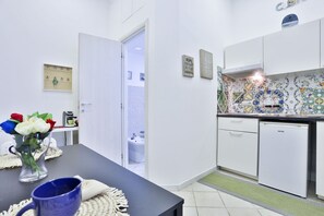 A compact kitchen with white cabinets, a small refrigerator, and a tiled backsplash. - GuestHost - Aunt Maria's Little House (Naples)