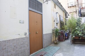 A narrow alleyway with a closed wooden door, a tiled wall, and a small potted plant. - A cozy apartment perfect for two people, located on the ground floor of a building near the Spanish Quarter, on the highest part of the hill and close to the Corso Vittorio Emanuele funicular. Comfortable and simple, with a direct entrance to the kitchen (Naples)