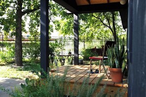 A covered patio area with a wooden deck, a metal fence, and potted plants. - Close to Downtown — The Cozy Bungalow (Austin)