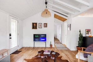 Ein modernes Wohnzimmer mit Holzboden, einem großen Flachbildfernseher, einer gewobenen Pendelleuchte und einer Kakteenpflanze.