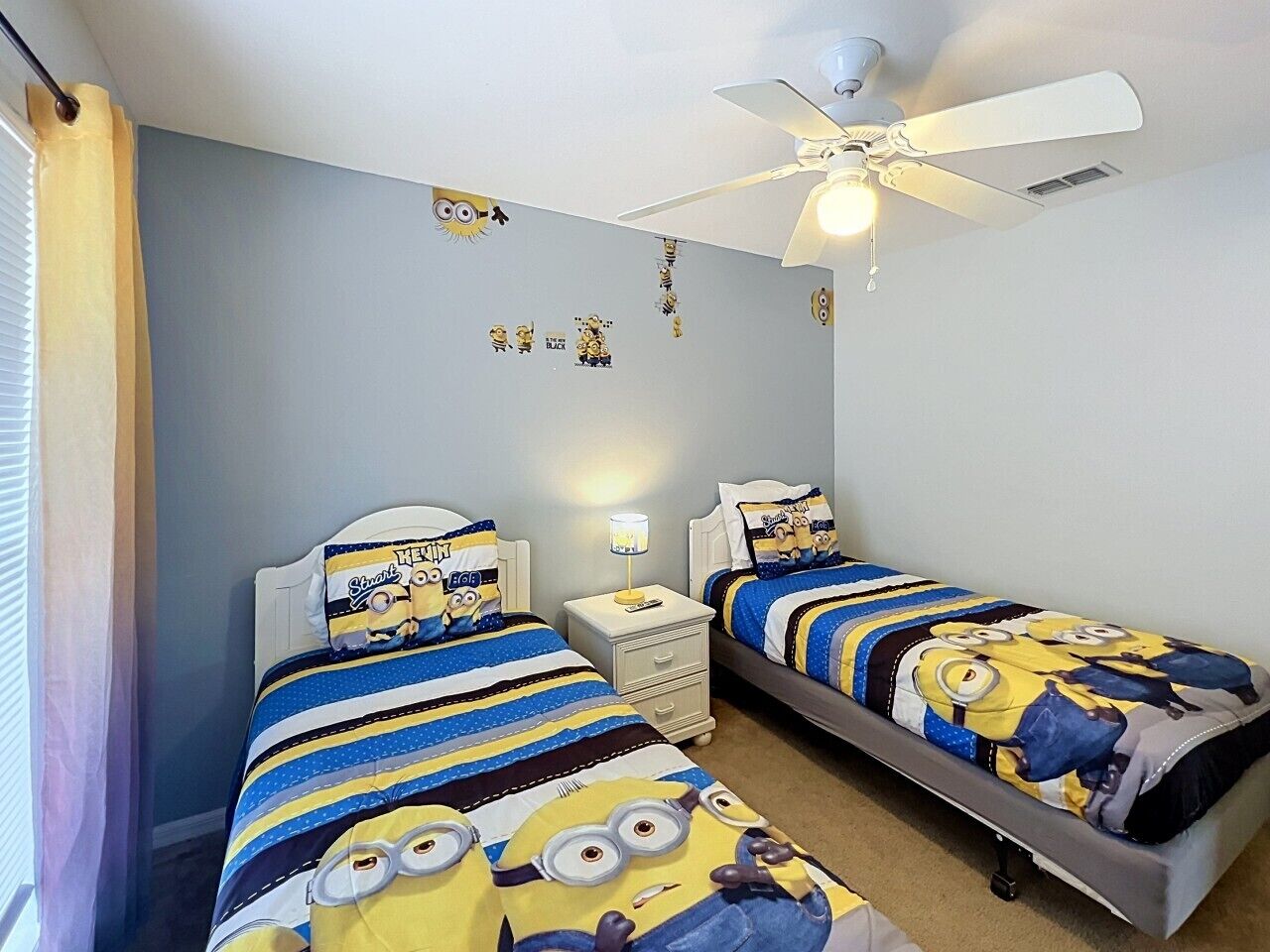 Un dormitorio con dos camas, ventilador de techo y mesita de noche con lámpara.
