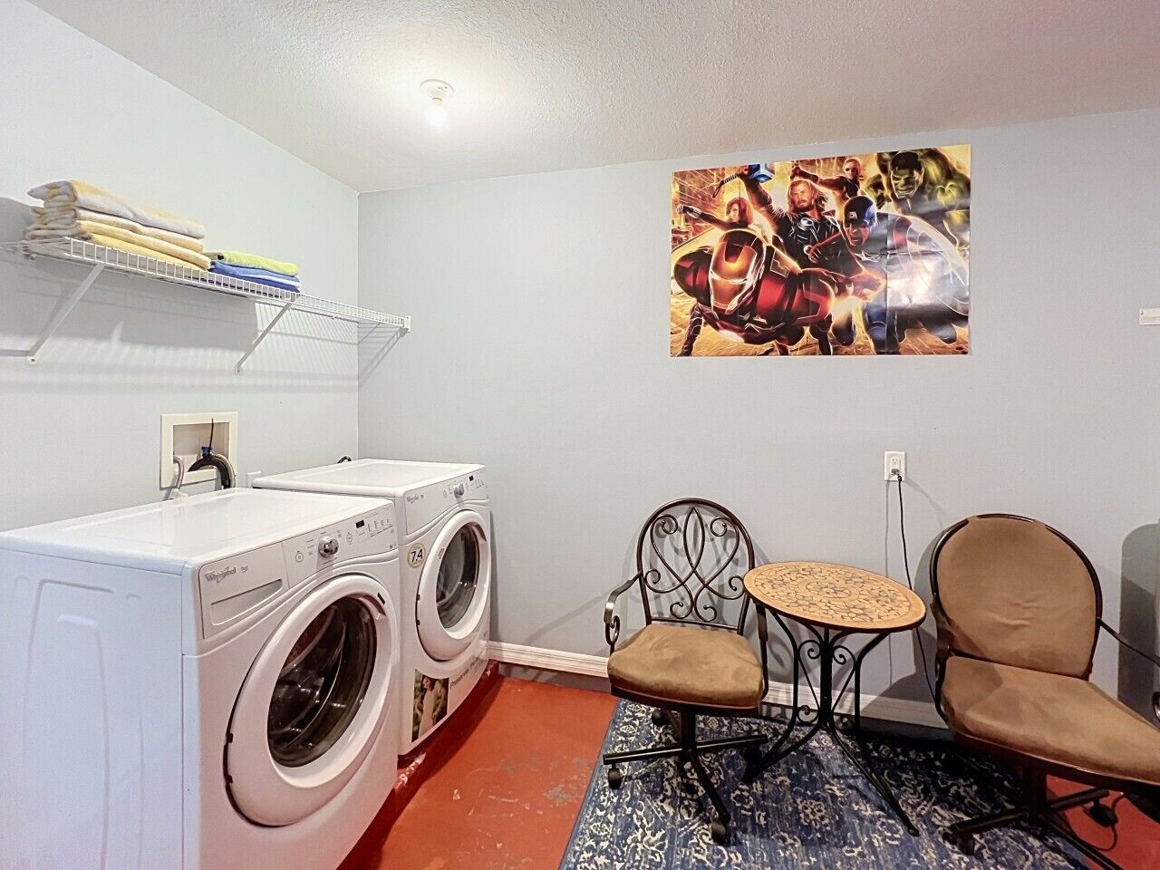 Un espace buanderie comprenant un lave-linge, deux chaises, une petite table et une étagère fixée au mur où sont pliées des serviettes.