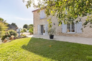 Une maison en pierre avec un jardin, une plante en pot et une voiture blanche garée devant.