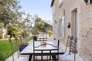 Une terrasse extérieure avec une table et des chaises, un bâtiment en pierre et un jardin avec des arbres et des plantes.