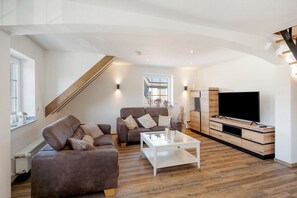 Ein modernes Wohnzimmer mit einer Sofagarnitur, einem Couchtisch, einem Fernseher und einer Treppe.