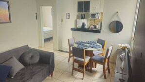A living room with a sofa, a dining table with chairs, a kitchen area with cabinets and appliances, and a bedroom visible through an open door. - Cozy and well-located apartment (Uberlândia)