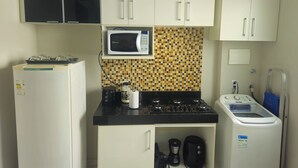 A compact kitchen with a refrigerator, microwave, stove, coffee maker, and washing machine. - Cozy and well-located apartment (Uberlândia)