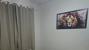 A bedroom with a bed, curtains, a wall-mounted painting, and a tiled floor. - Cozy and well-located apartment (Uberlândia)