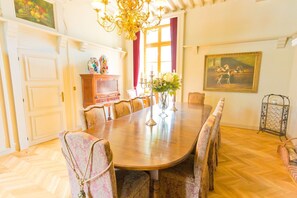 Ein Esszimmer mit Holztisch, gemusterten Stühlen, einer Chandelierleuchtre, einem Schrank und einem Gemälde an der Wand.