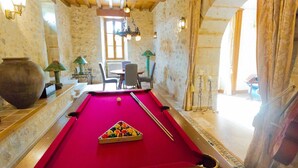 A pool table with balls, a large vase, and a table lamp in a room with stone walls and wooden beams.