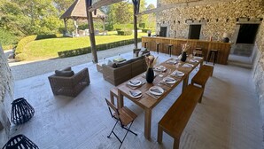 An outdoor dining area with a stone wall, a wooden table set for six, and a stone fireplace.