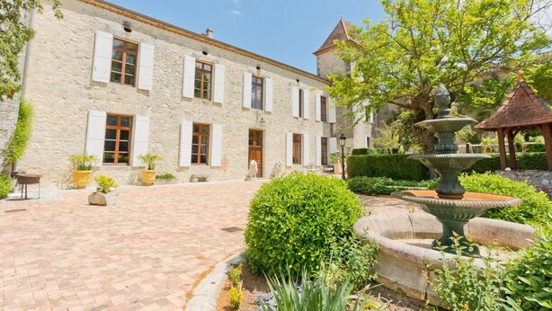 A stone building with multiple windows and a courtyard with a fountain and greenery.