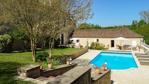 A poolside area with a pool, outdoor furniture, and a building with a tiled roof.
