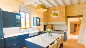 A kitchen with dark blue cabinets, a white marble countertop, a large island with seating, and a brick wall.