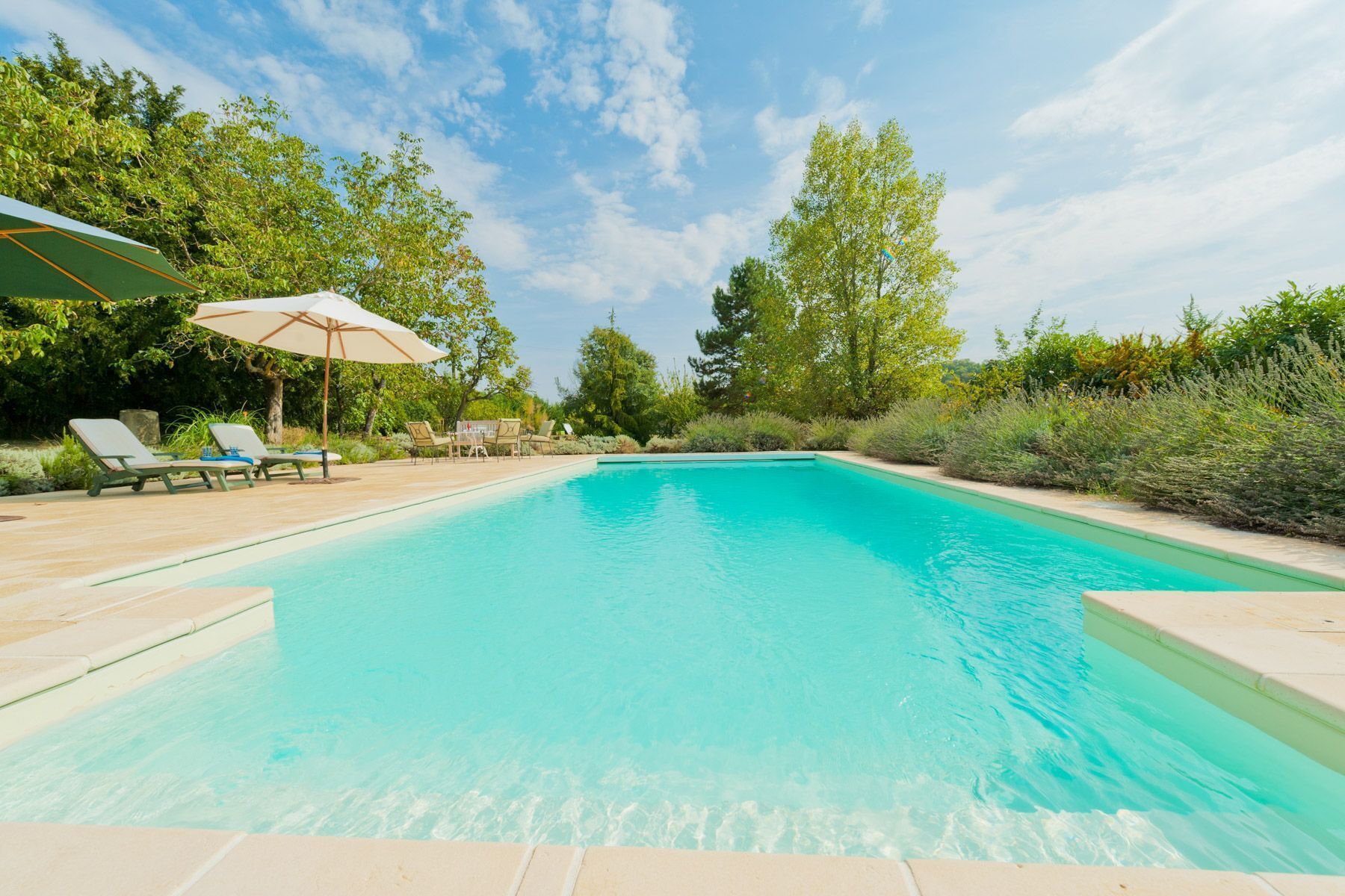 A rectangular swimming pool with clear blue water, surrounded by a wooden deck.